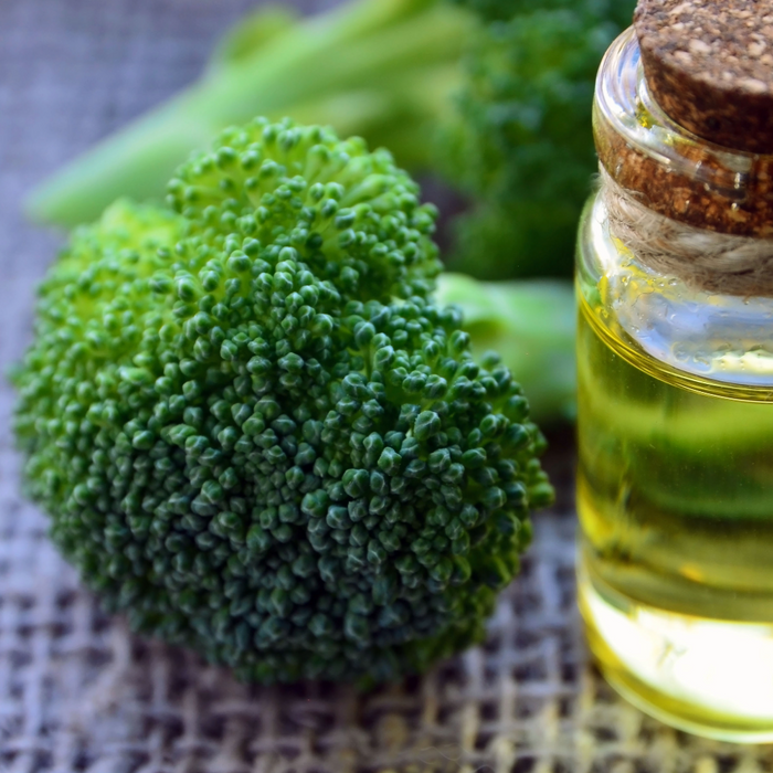broccoli floret beside a glass vial of broccoli seed oil, which is a light yellow-green colour