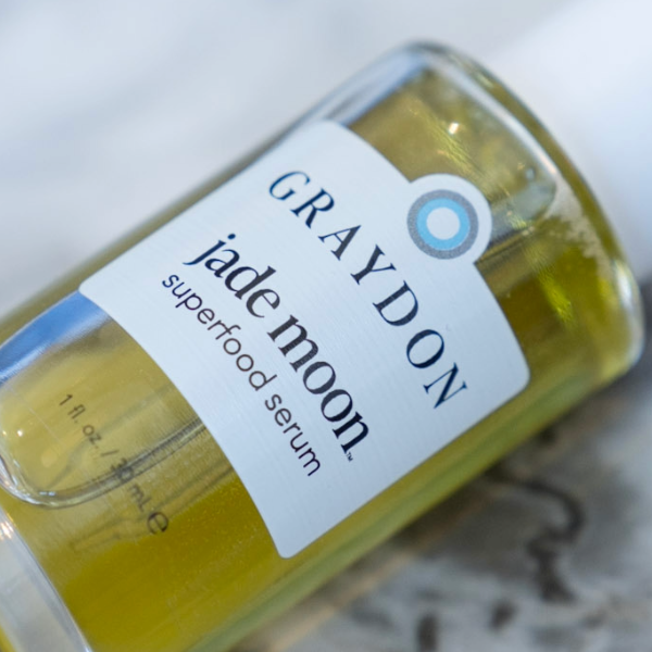 a photo of a full green-yellow bottle of jade moon serum on a marble backdrop